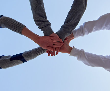A low angle shot of three young friends putting their hands together against a blue sky