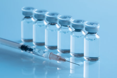 A closeup shot of covid19 vaccine bottles with a needle on a blue background - covid19 conceptの写真素材