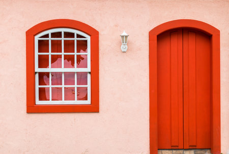 A red wooden door and a window on the facade of a houの写真素材