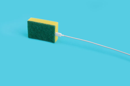 A closeup of a USB cable plugged in a kitchen sponge isolated on a pastel blue backgroundの写真素材