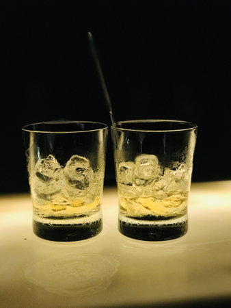 A vertical shot of two glass cups of whisky with ice on the tableの写真素材