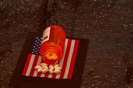 An American opioid crisis concept. Prescription bottle with pills on a black background and American...