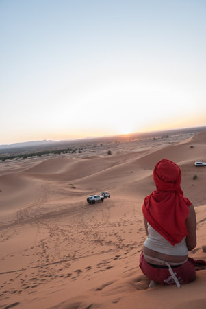 A rear view of a Moroccan woman sitting on the sandy desert in Merzouga, Moroccoの写真素材