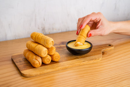 Venezuelan tequenos cheese fingers piled high on a wooden table and hand with tequeno dipping it in the sauce.の写真素材