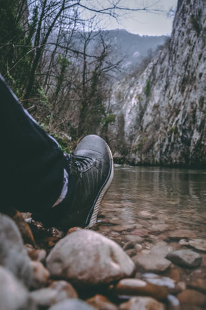 A selective focus of the shoe of a hiker on the rocky riverside near mountainの写真素材