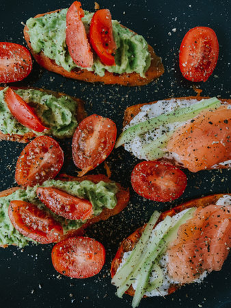 a top view of red tomatoes and green and white cream on meat on a black backgroundの写真素材