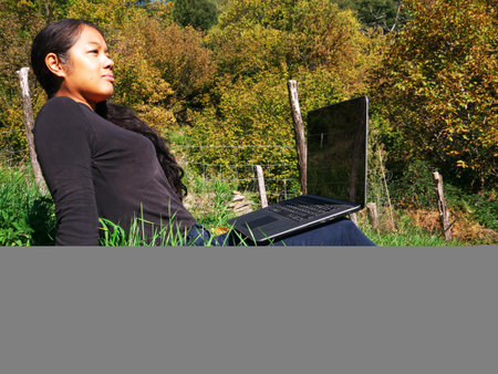 Young black woman sitting on the grass with her computer working. Profile viewの写真素材