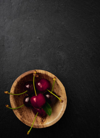 A vertical shot of fresh juicy cherries in a small wooden bowl isolated on a black backgroundの写真素材