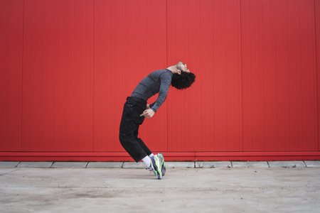 An athletic cool European guy posing outdoors in front of a red wall