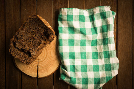 A green and white checkered tablecloth, a piece of bread, and a wood stump on a wooden surface