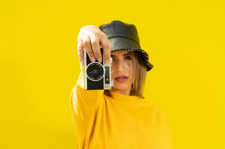 A closeup shot of a young Caucasian lady in yellow holding a photo cameraの写真素材