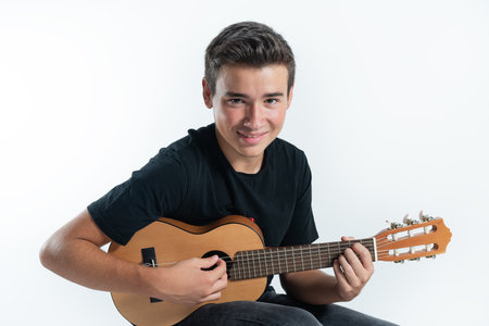A Spanish Caucasian teenage boy playing the ukulele while sitting, in front of a white background
