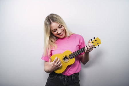 A young cheerful Caucasian female from Spain playing ukulele against a white wallの写真素材