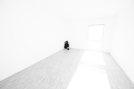 Depressed Woman Sitting on the Floor in a Corner in a Empty Room at Home in Switzerland.の写真素材