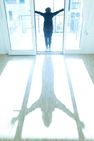 Woman Standing with Arms Outstretched on the Floor in a Empty Room with Sunlight at Home in Switzerland.の写真素材