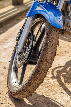 A closeup shot of a muddy motorcycle wheel after a race on a sunny day