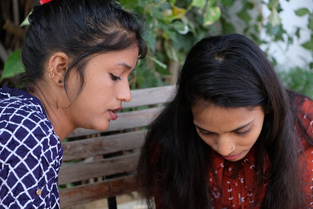 Two Indian female friends sitting on a bench and looking through a phoneの写真素材