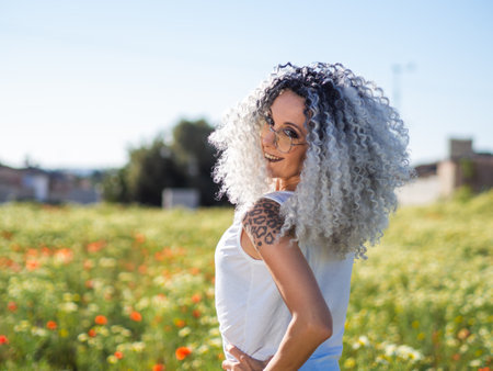 A sexy Spanish woman with white curly hair and tattoos posing in a meadow in a light summer outfitの写真素材