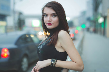 A young brunette female in a leather jacket posing leaning on a railing in a street