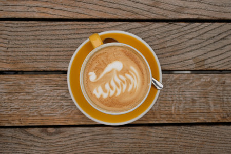 A top-view of a cup of cappuccino with latte art at the midpoint of a wooden tableの写真素材