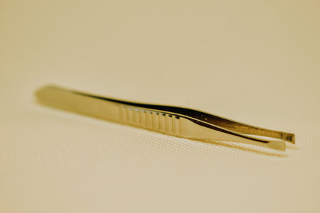 a closeup of golden tweezers on a beige backgroundの写真素材