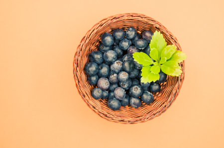 A top view of blueberries and a leaf in a basket on an orange backgroundの写真素材