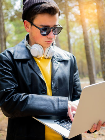 A teenager in headphones and sunglasses working on a laptop computer in a parkの写真素材