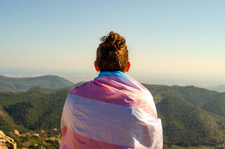 Picture of Young Long Hair  Man With Topknot Back Sitting at Mountains Canyon Looking to Horizon in Nature with Transgender LGTB Flagの写真素材