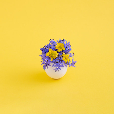 A closeup shot of an eggshell with beautiful colorful flowers isolated on the yellow backgroundの写真素材