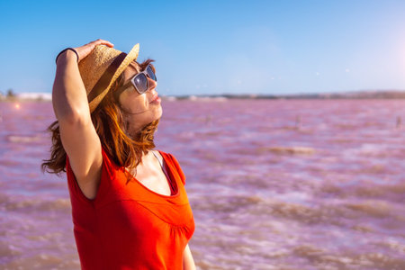 A girl enjoying the summer with a red dress and straw hat in the pink lagoon of Torrevieja,...