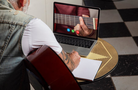 Man jotting down notes in notebook while taking online classes on laptop. Online training, online classes.の写真素材