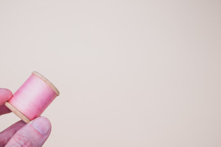 A hand holding a pink sewing thread isolated on a light background with free space for textの写真素材