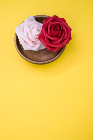 A vertical shot of pink and red roses in a wooden bowl on a yellow backgroundの写真素材