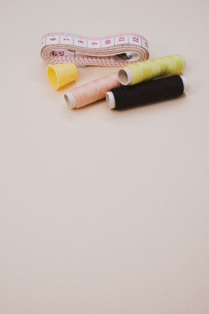 A closeup of the colorful  sewing threads with a thimble and a measuring tape on the brown surface