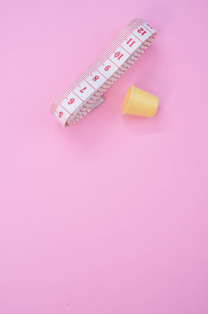 A closeup of a measuring tape with a plastic thimble on the pink surface - space for textの写真素材