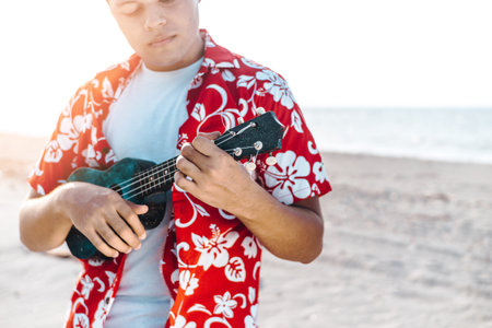 portrait of a young latin american man holding and playing a stringed instrument or ukulele. chords and music concept.の写真素材