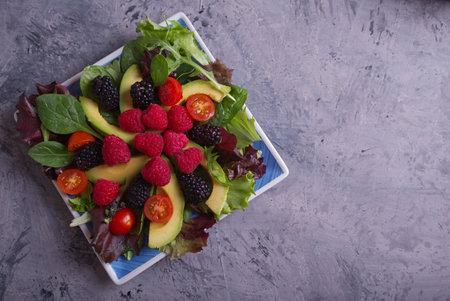 Salad with red berries, cherry tomatoes and avocado, on a gray table.