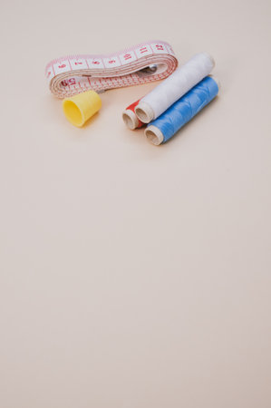A closeup of the colorful  sewing threads with a thimble and a measuring tape on the brown surface