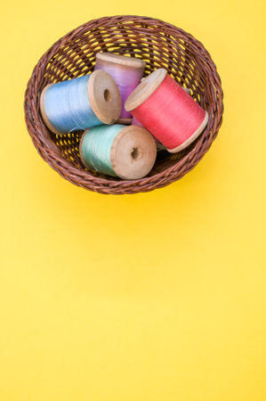 A basket of colorful sewing threads isolated on a yellow background with free space for textの写真素材