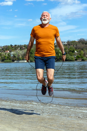 Active senior elderly man jumping the rope, exercising on the beach by the riverbank. Motion blur.の写真素材