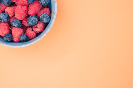A bowl of fresh blueberries and raspberries isolated on an orange background with space for textの写真素材
