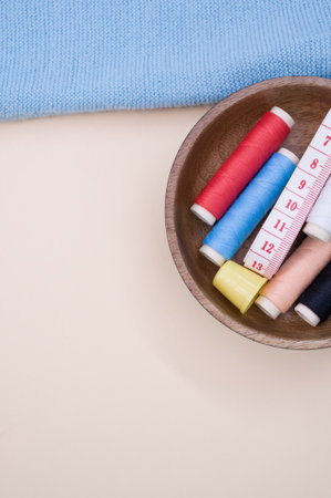 A top view of the colorful sewing threads with a thimble and a measuring tape in the wooden bowl