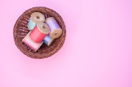 A basket of colorful sewing threads isolated on a pink background with free space for textの写真素材