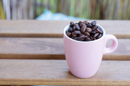 A closeup shot of coffee beans in a pink cup on a wooden surfaceの写真素材
