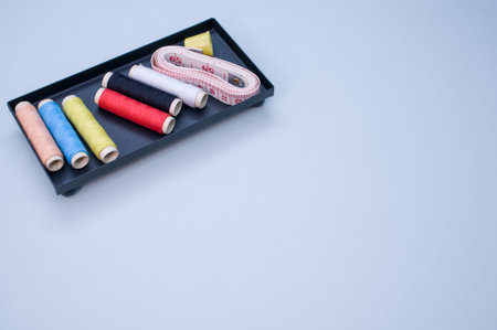 A pack of colorful sewing threads and a measuring tape on a blue background with a copy space