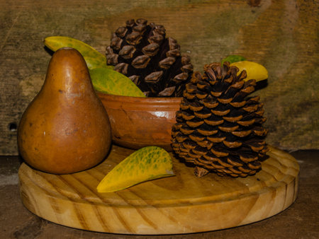 A wooden round board with pine cones, a pear, and leaves on itの写真素材