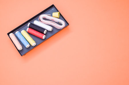 A pack of colorful sewing threads and a measuring tape on orange background with a copy spaceの写真素材