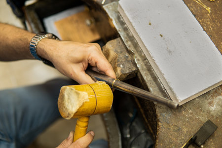 Close up view of a Jeweler working in his workshop repairing a gold ring with a wooden hammer