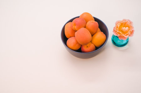 A studio shot of apricots in a bowl and a flower decoration