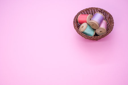 A basket of colorful sewing threads isolated on a pink background with free space for textの写真素材